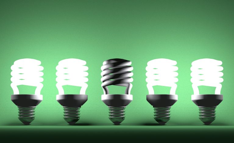 Dead spiral lightbulb in row of glowing ones on green